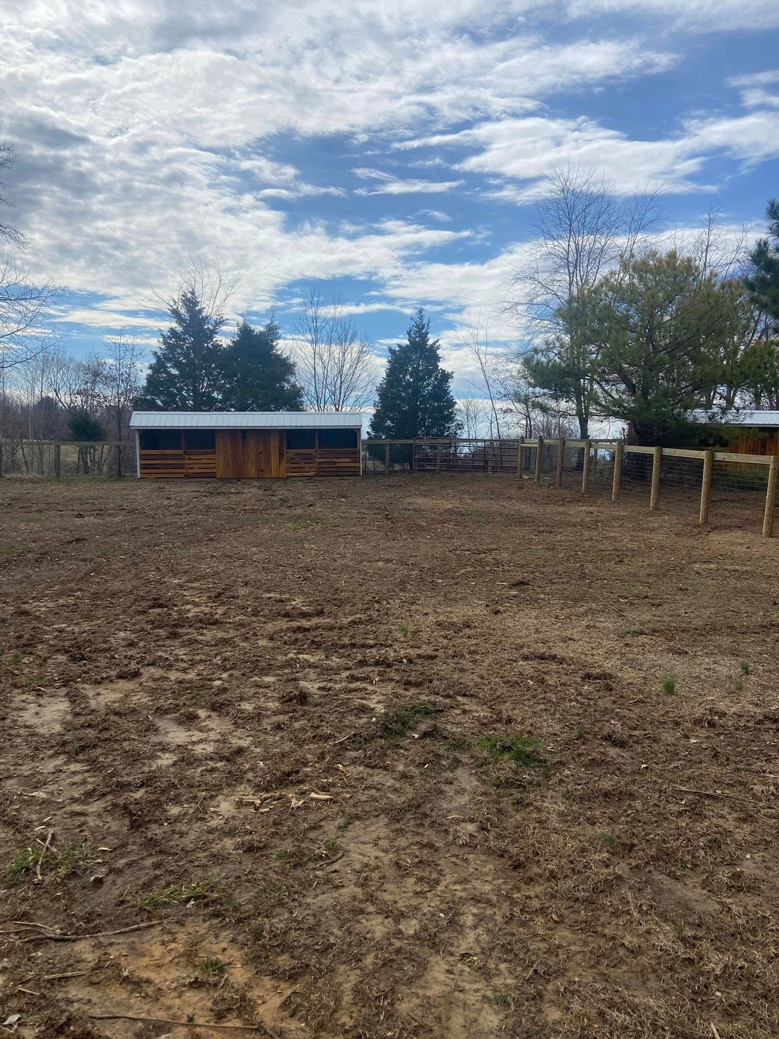Muddy pen with shed and fence under cloudy sky.
