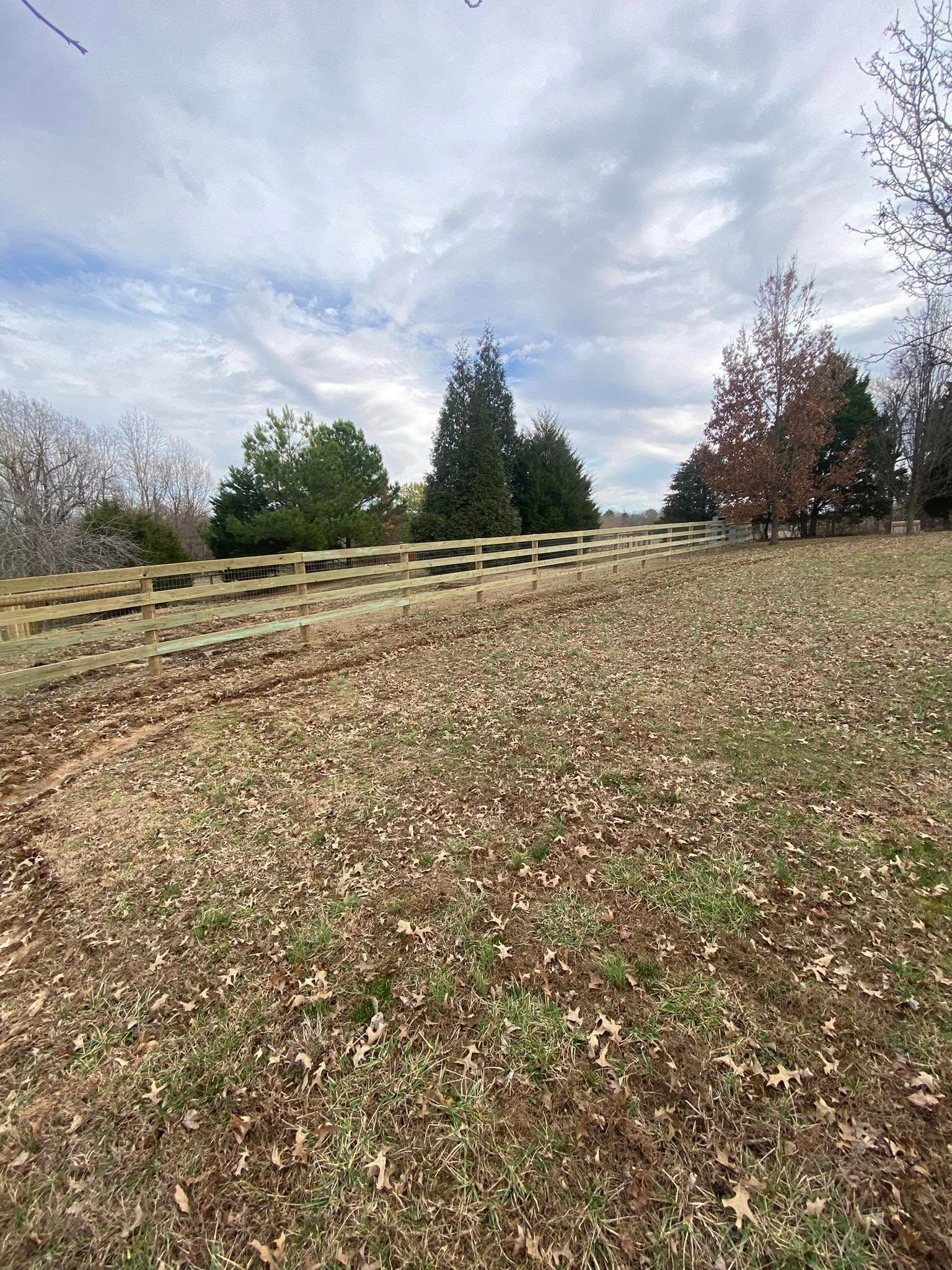 Wooden fence in a field with fallen leaves under a cloudy sky.