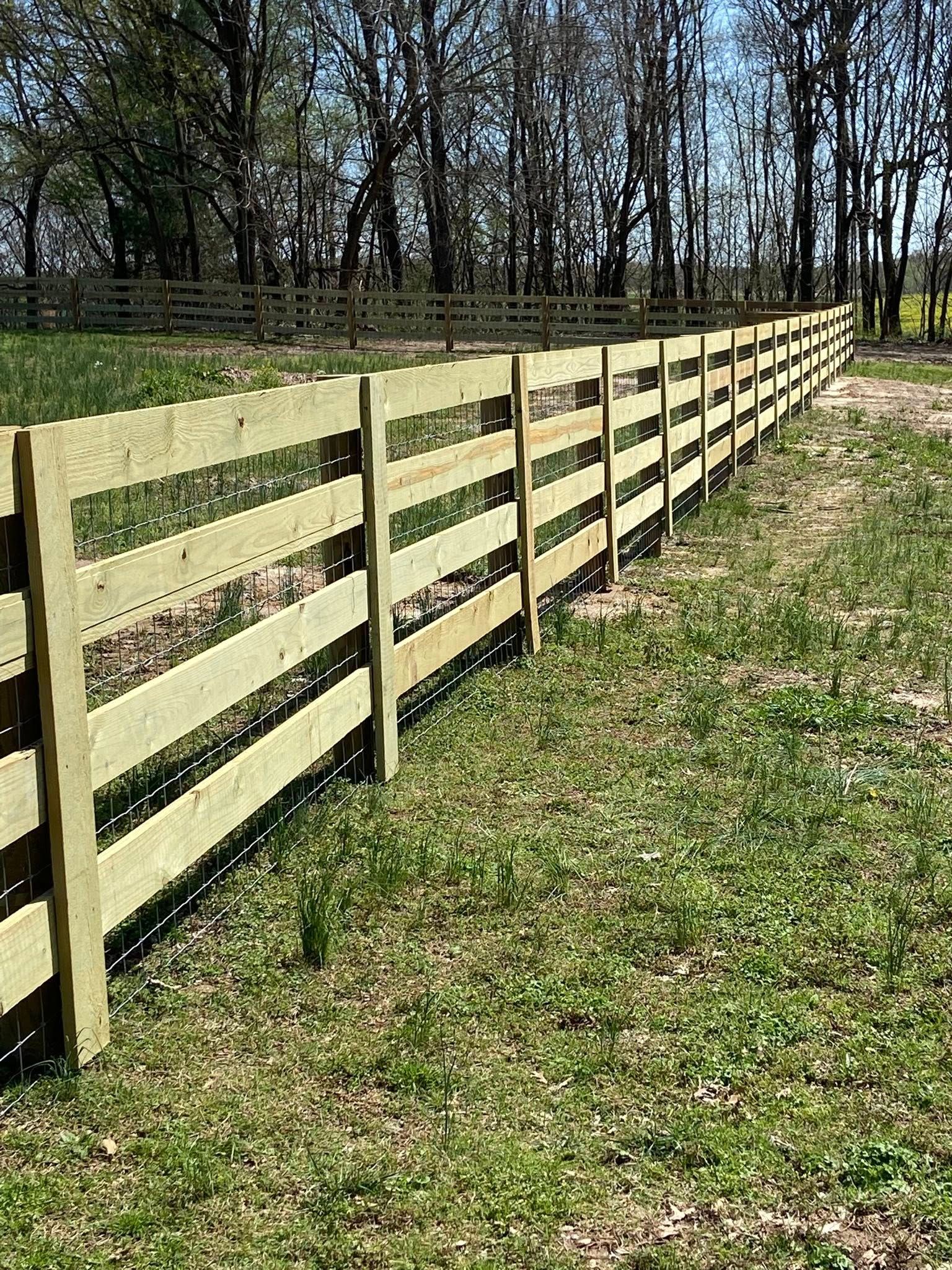 Wooden fence in a grassy field, trees in the background, sunny day.