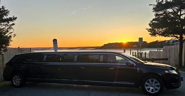 A black limousine is parked in front of a body of water.