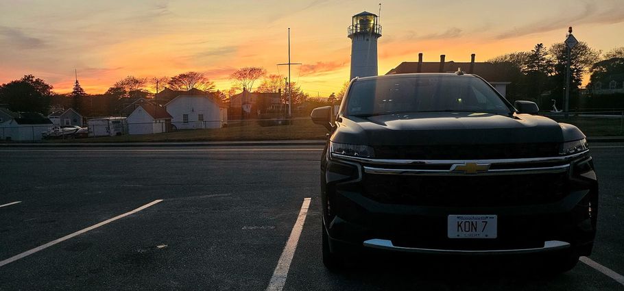 A black car is parked in a parking lot at sunset.
