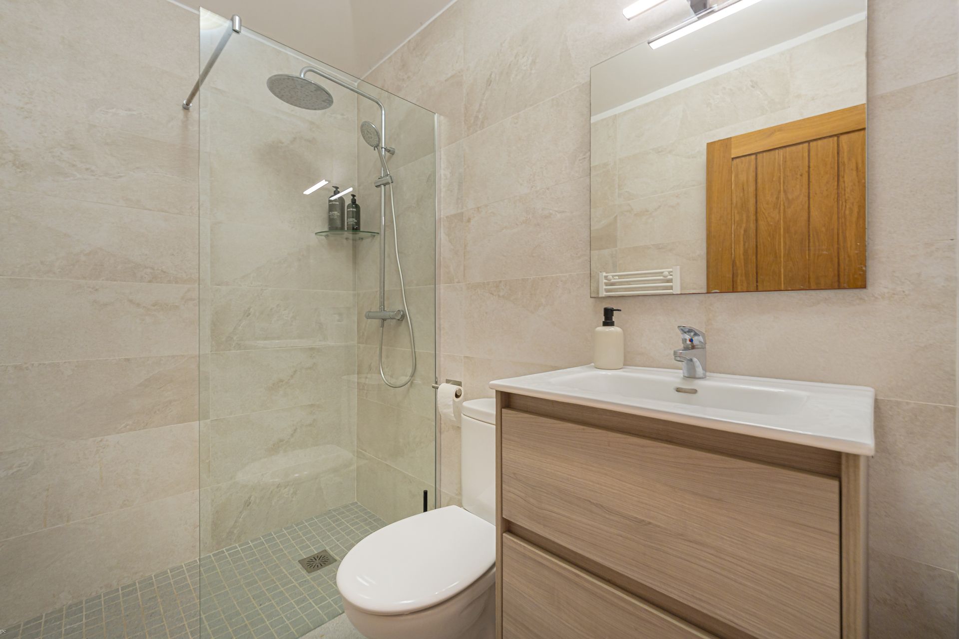 Moderne badkamer met glazen douchecabine, toilet en houten wastafelmeubel met spiegel.