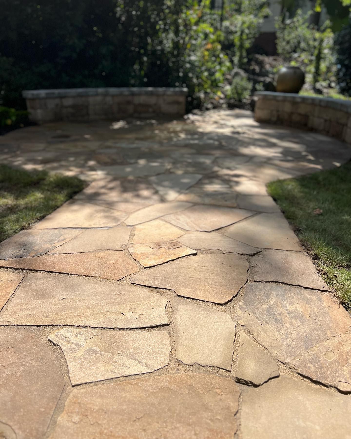 Stone garden path leading to a curved patio wall surrounded by greenery