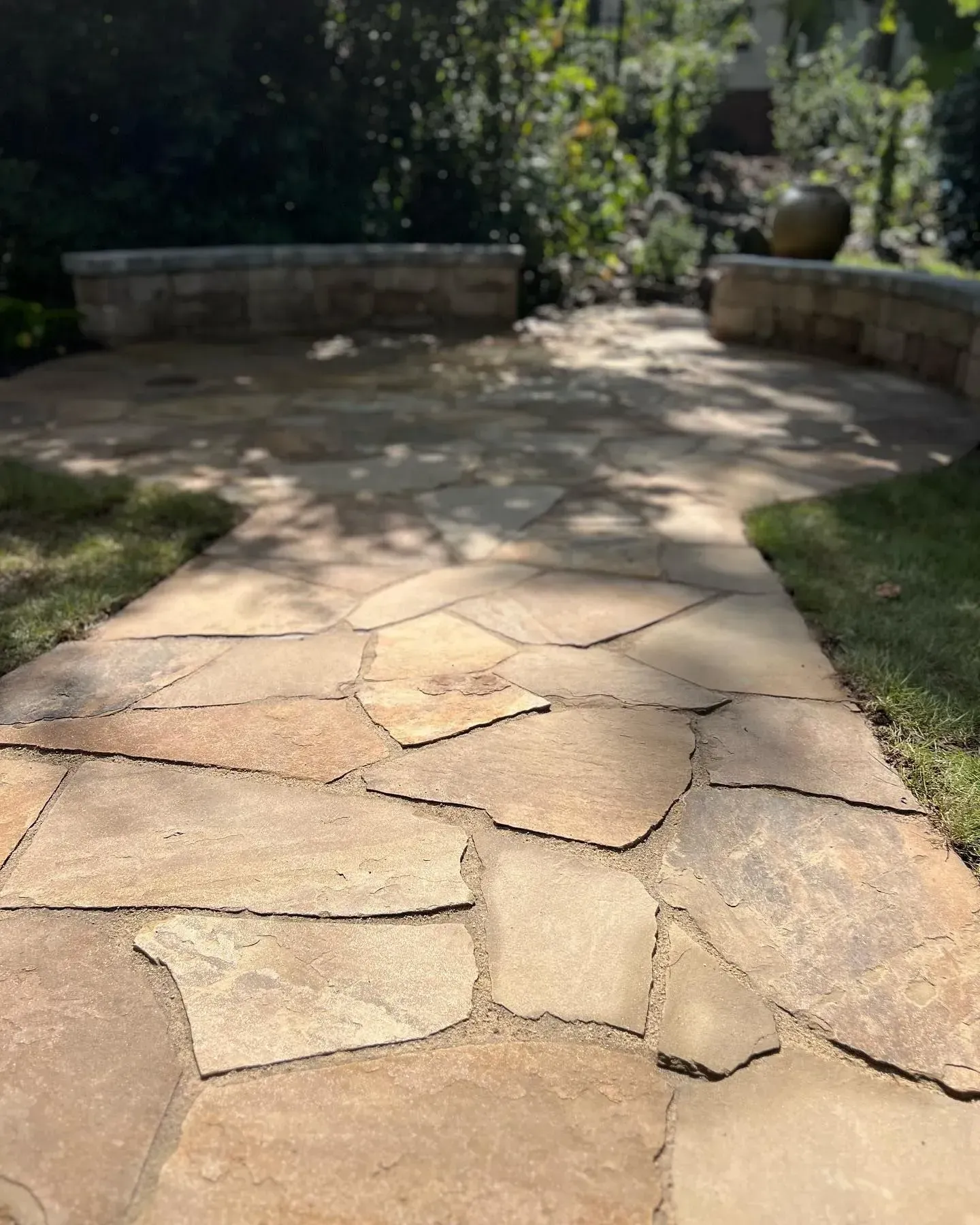 Stone pathway leading to a sunlit garden patio with low stone benches and greenery