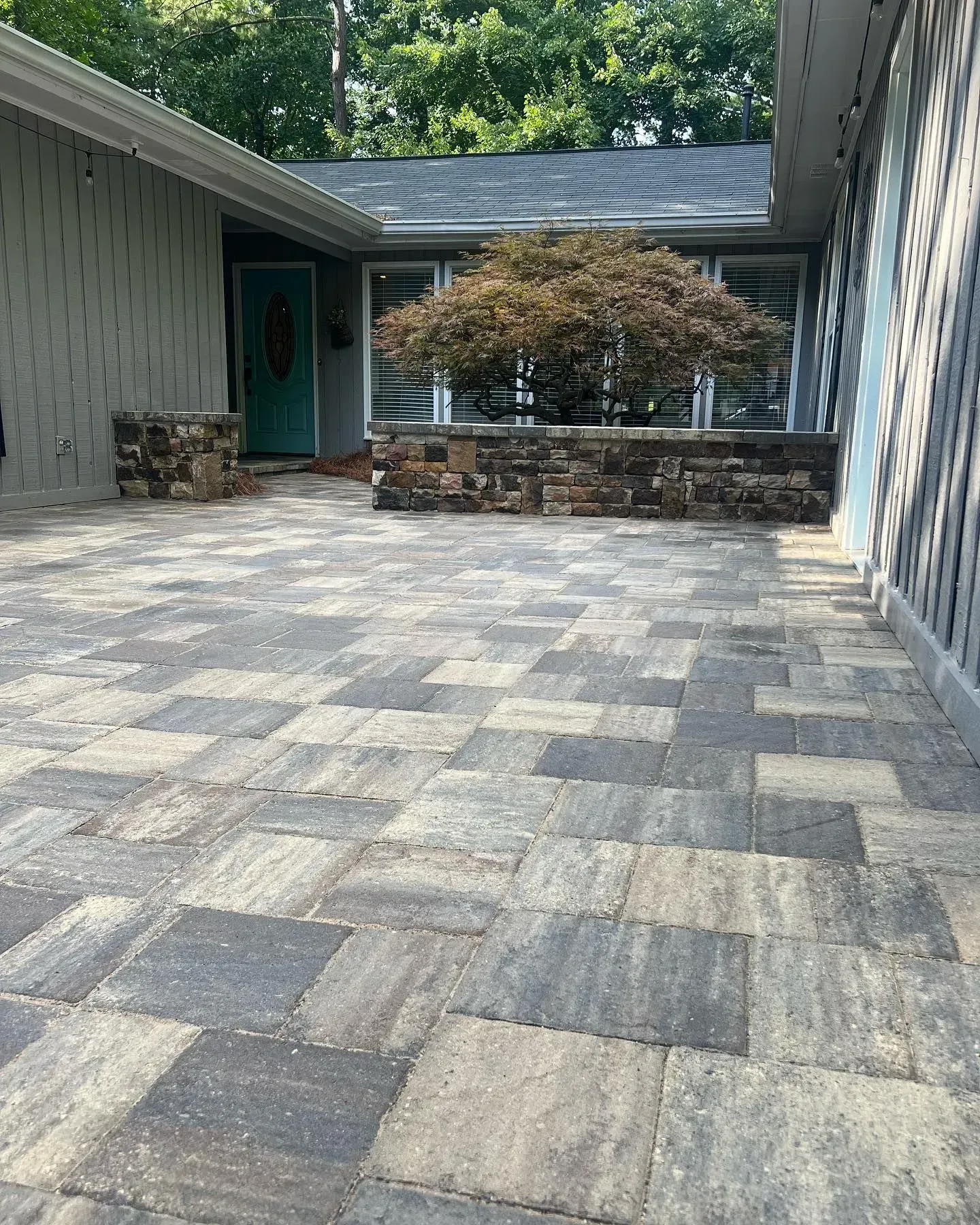 Stone patio beside a house with gray siding, a covered walkway, and a low stone wall