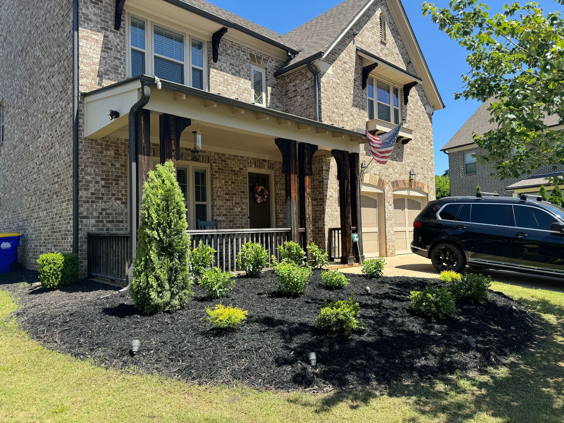 Brick suburban house with front porch, black SUV, and landscaped yard under a clear sky