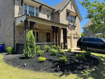 Suburban two-story brick house with a covered porch, black SUV, and landscaped front yard under a sunny sky