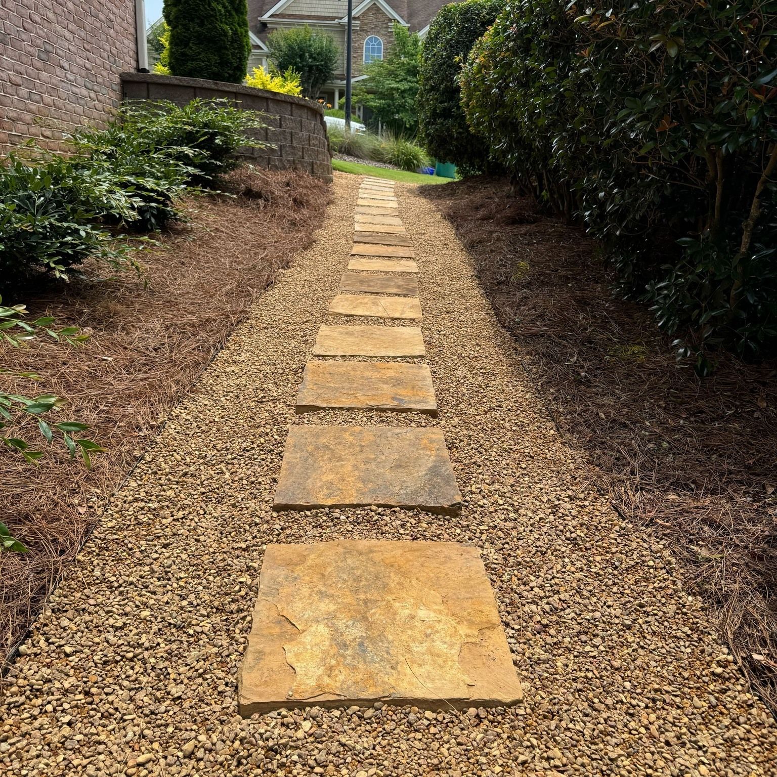 Stone stepping path through gravel in a landscaped garden, bordered by shrubs and brick walls