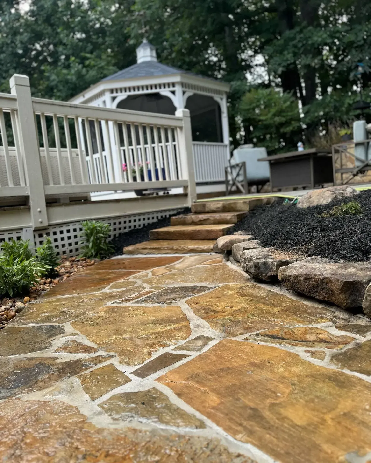 Stone walkway leading to a white gazebo in a wooded backyard