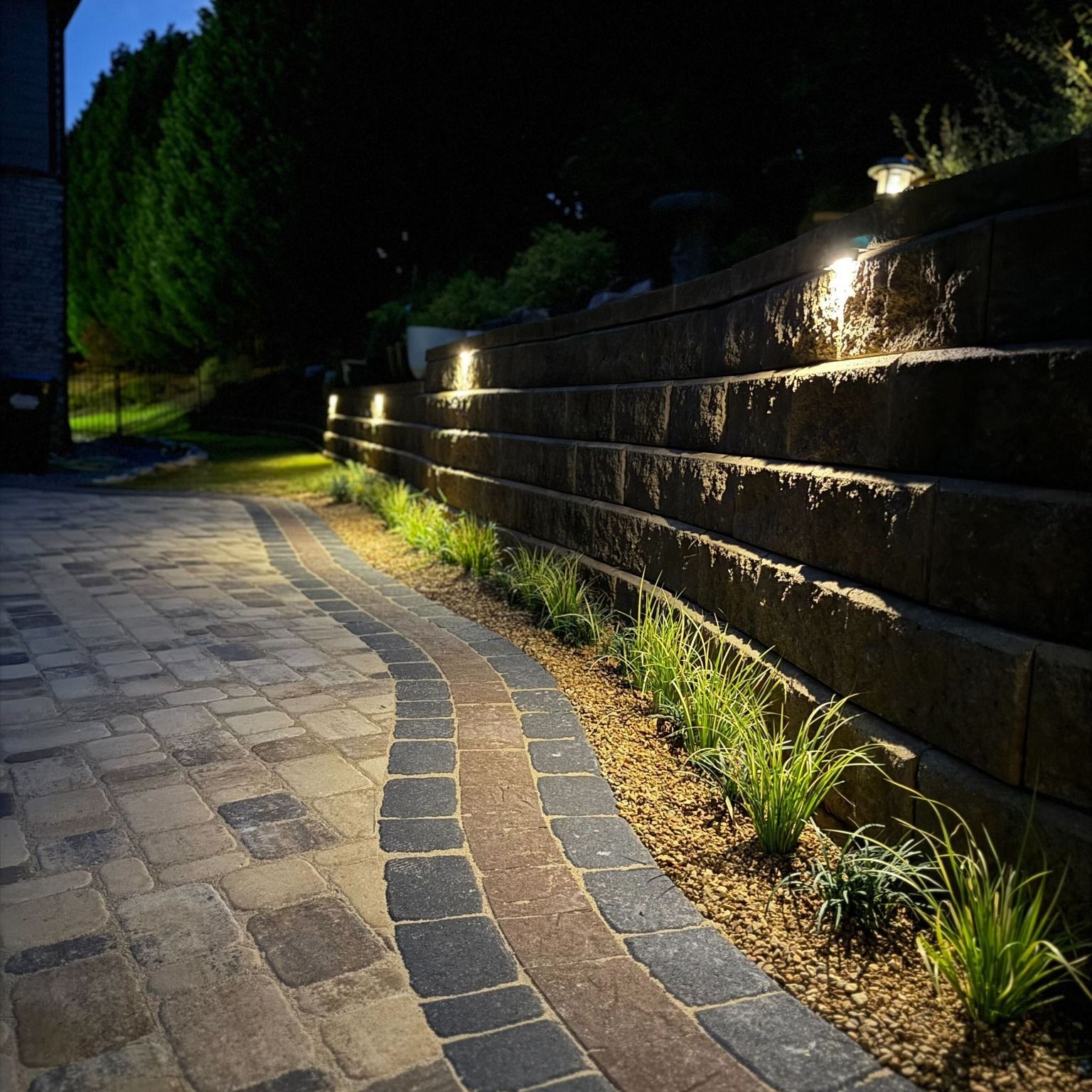 Curved stone walkway beside a lit retaining wall at night