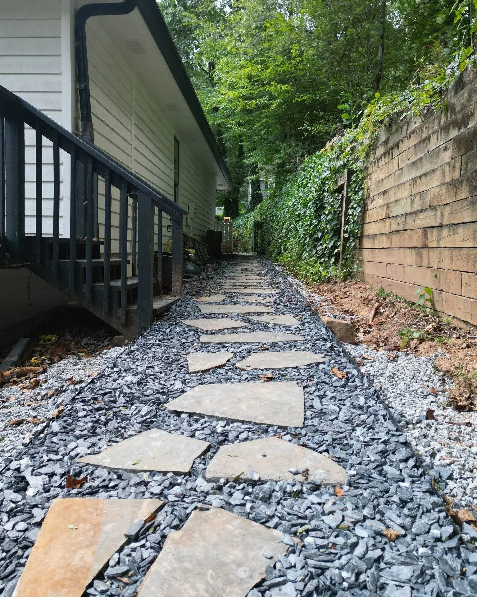 Stone walkway beside a house and retaining wall, lined with gravel and greenery