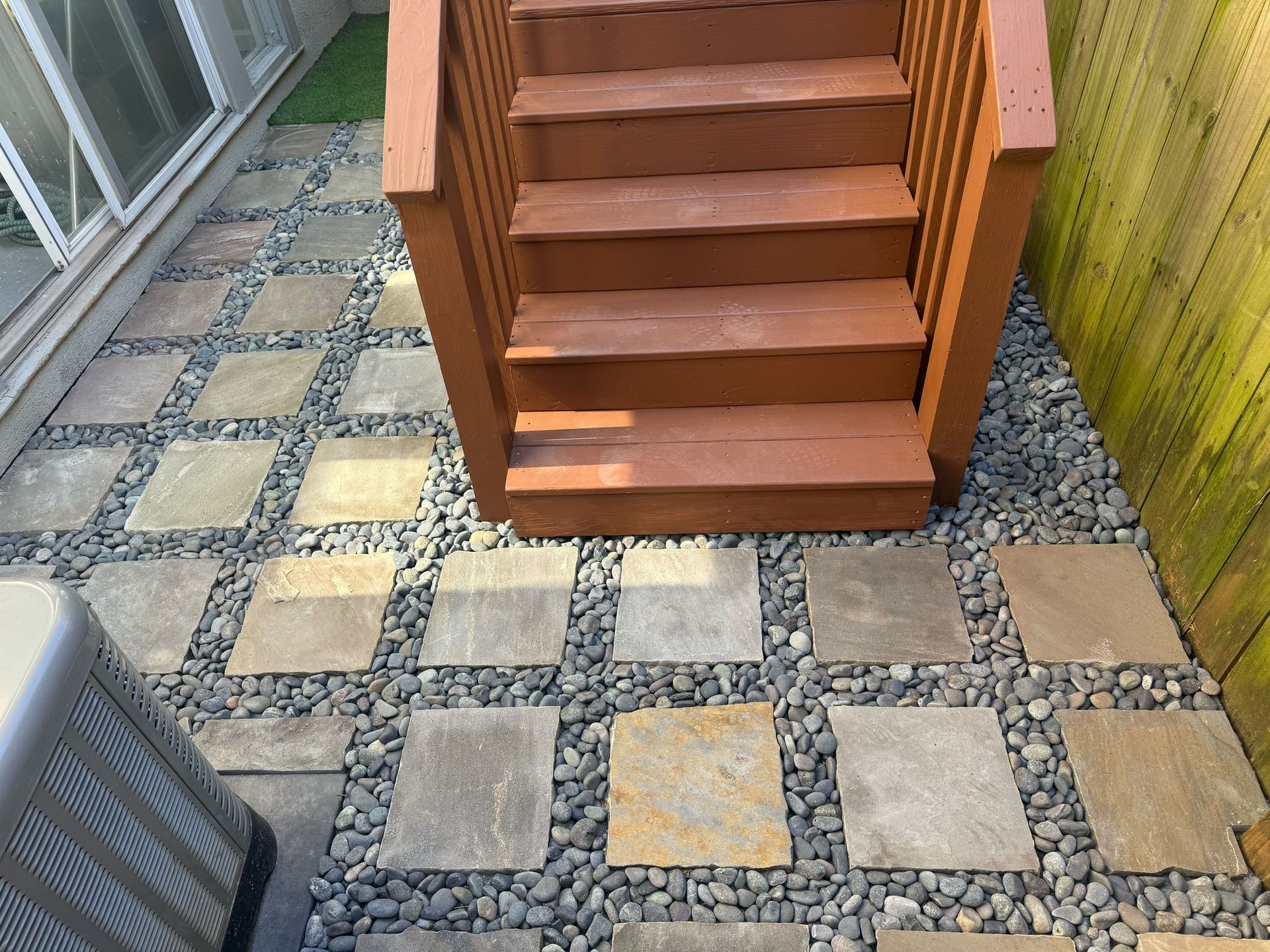 Outdoor patio with patterned stone pavers and wooden steps beside a building and railing