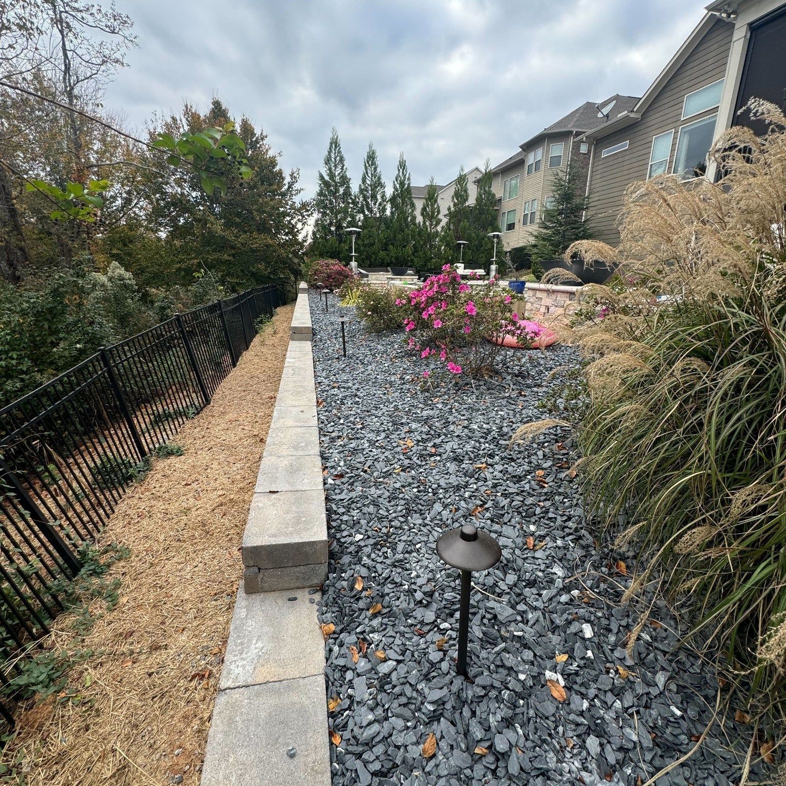 Residential front garden with gray rock bed, pink flowers, stone edging, and black fence