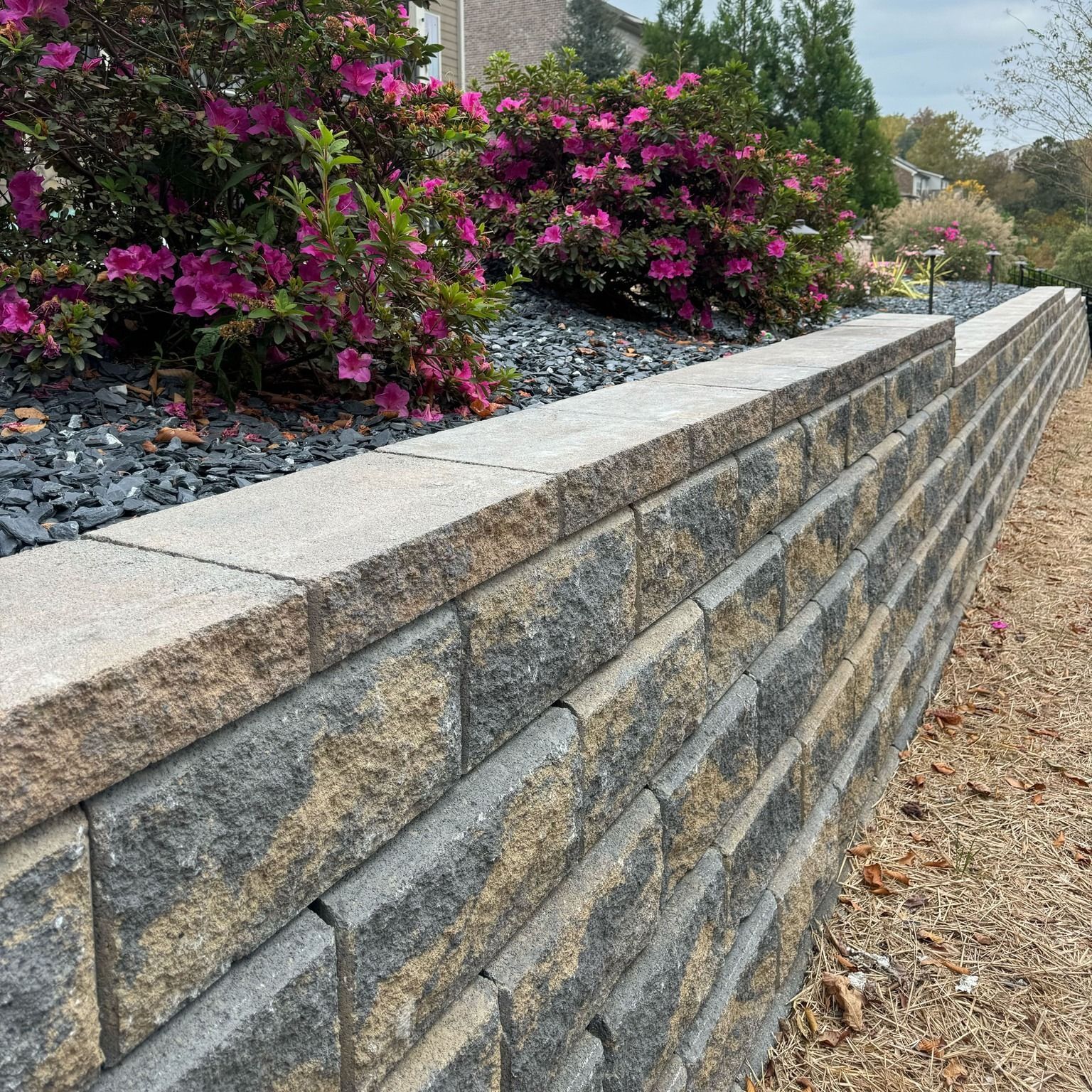 Stone retaining wall beside a landscaped bed with pink flowers and gravel path
