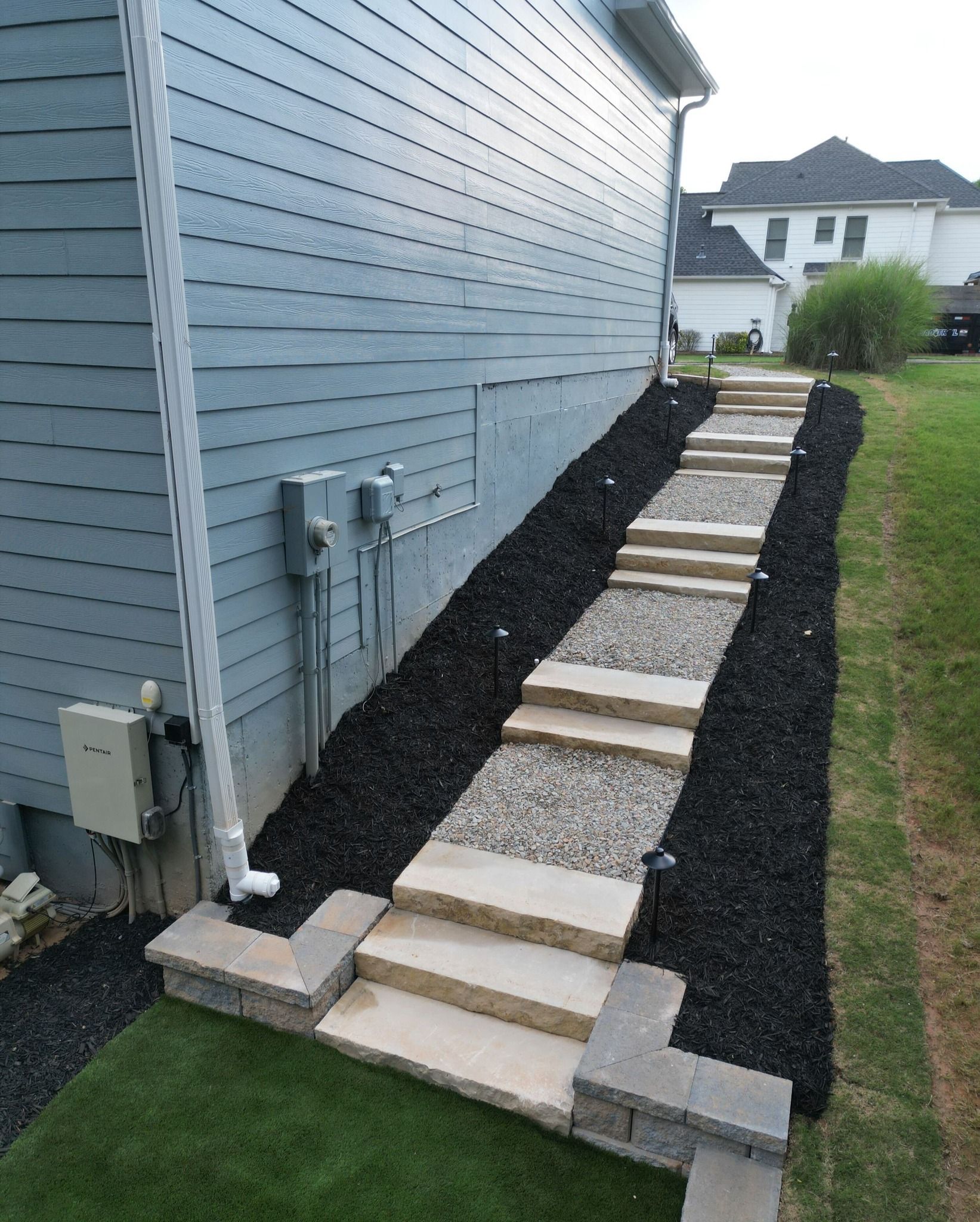 Stepped stone path beside a blue house, with gravel borders and grass lawn