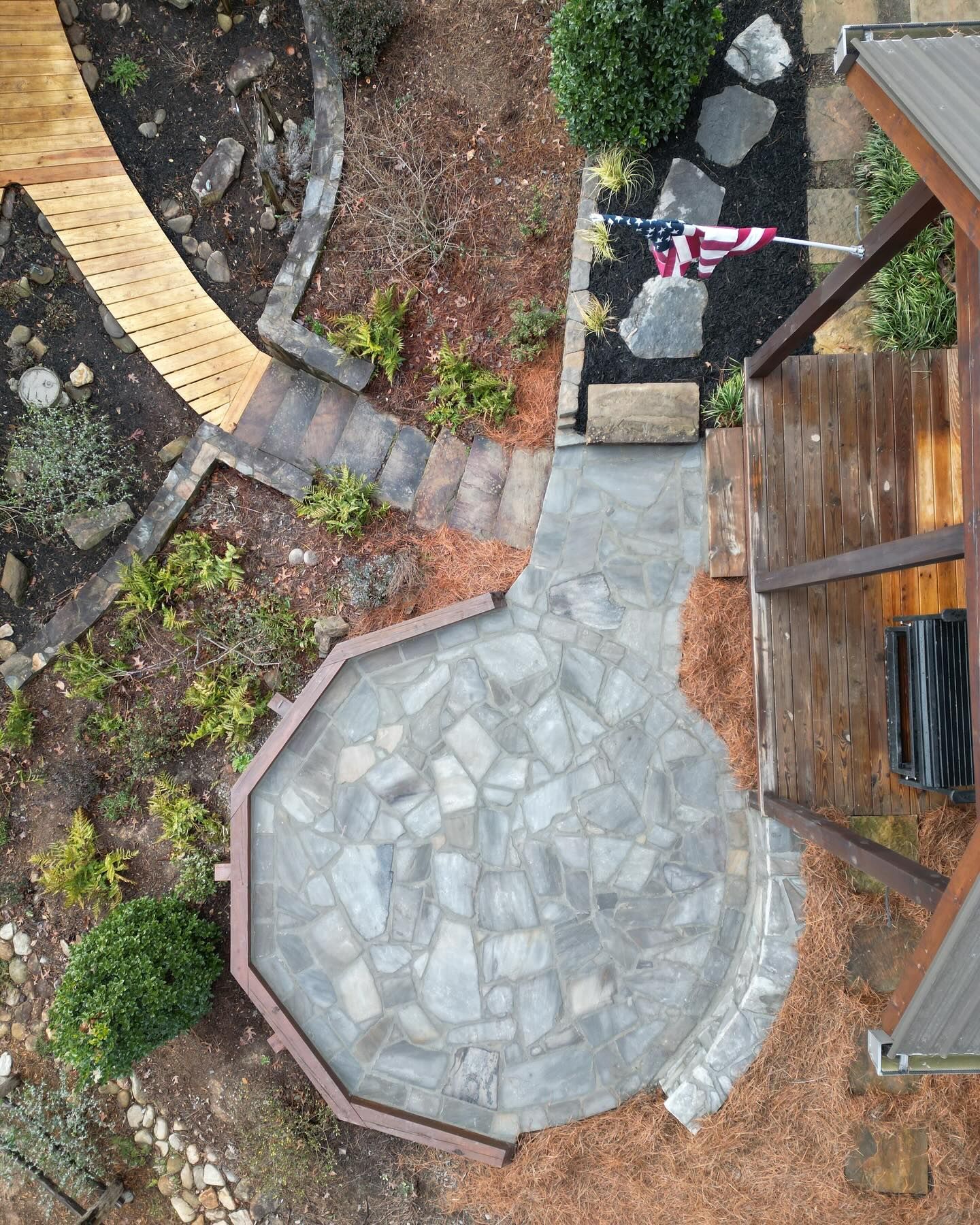 Backyard patio with stone pavers, garden beds, and a clothesline beside a wooden deck
