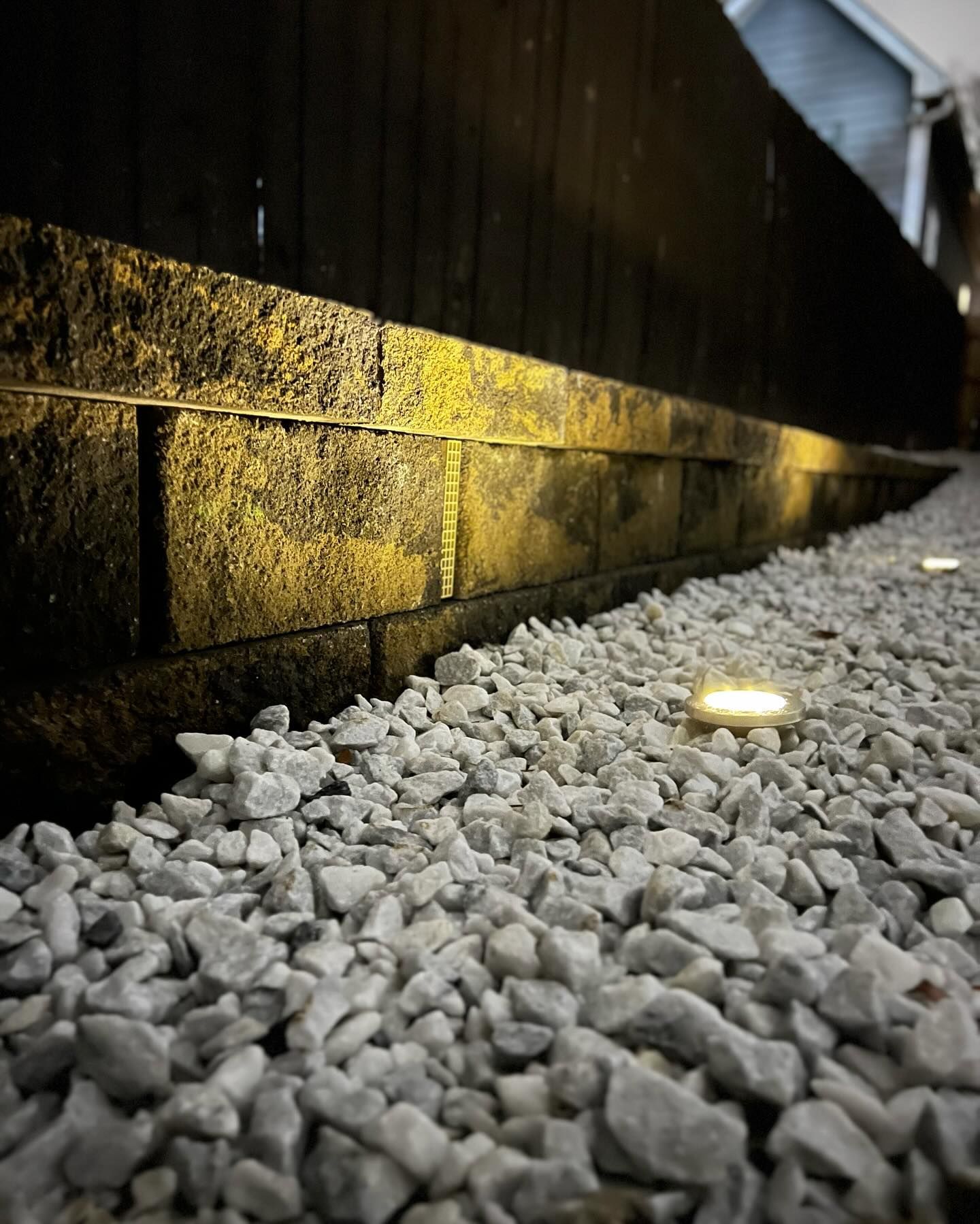 Low-angle view of gravel beside a glowing ground light and a dark wall at night