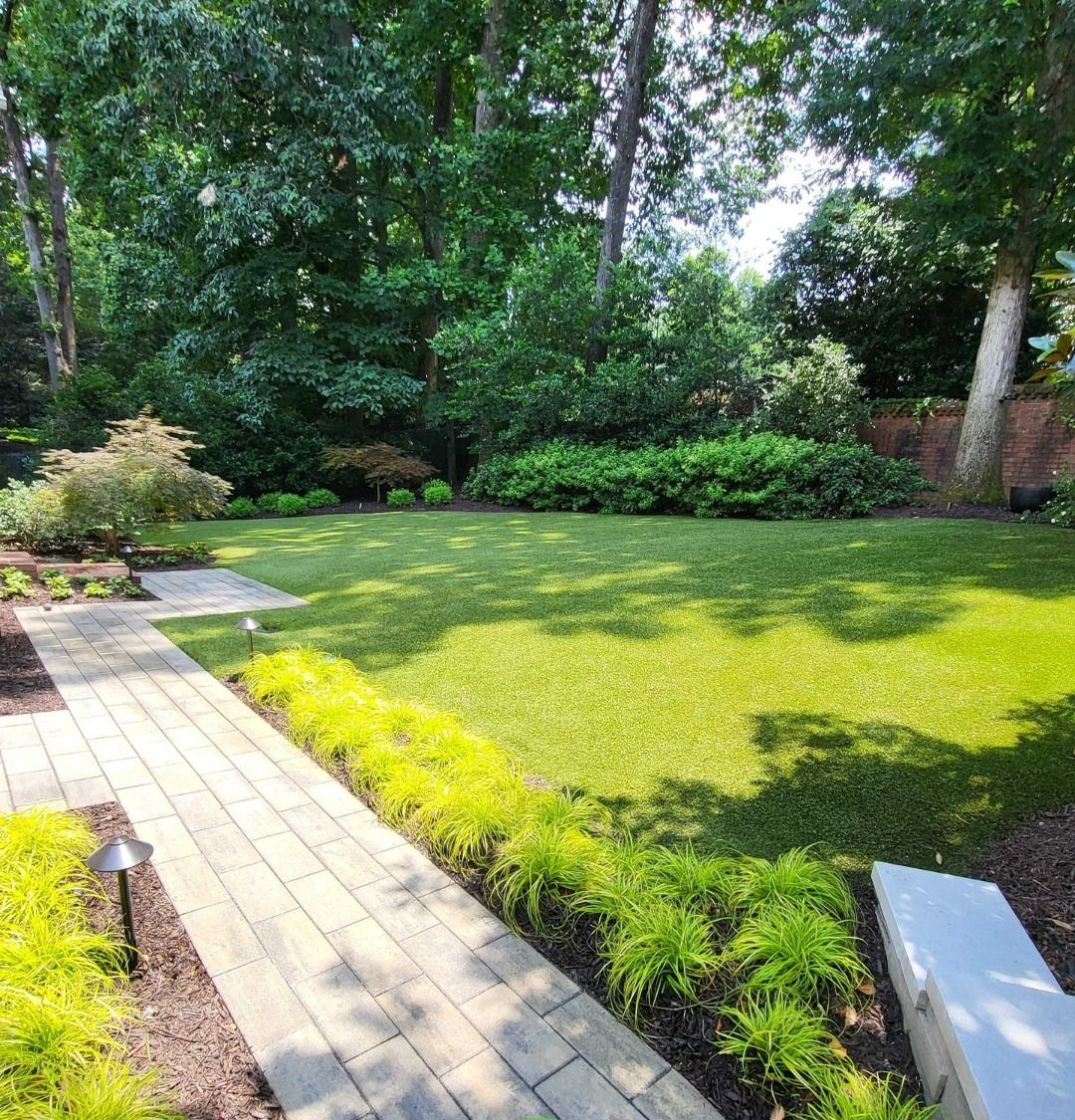 Lush green lawn with a stone walkway, bordered by plants, leading into a well-manicured backyard.
