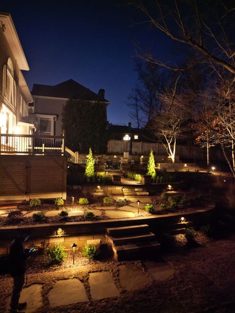 Nighttime landscaped backyard with stone steps, lit plants, and a house exterior on the left