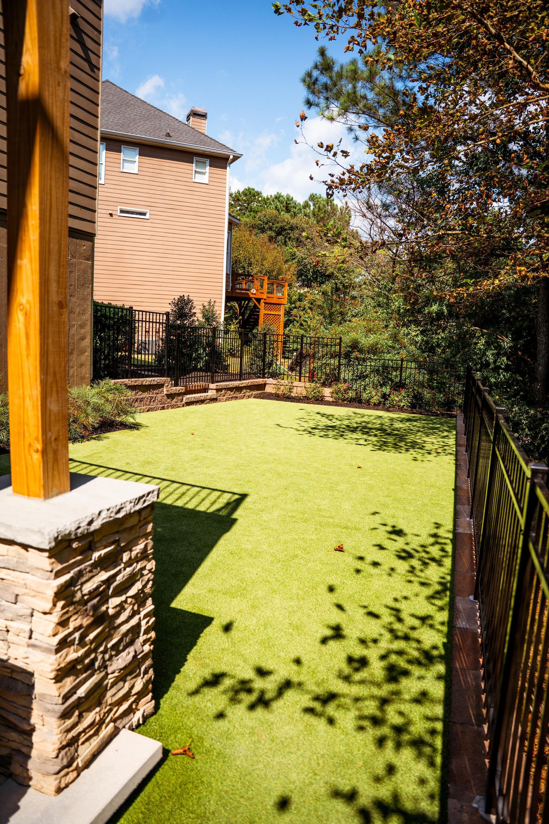 Backyard patio with bright green lawn, brick house, and autumn trees in sunlight