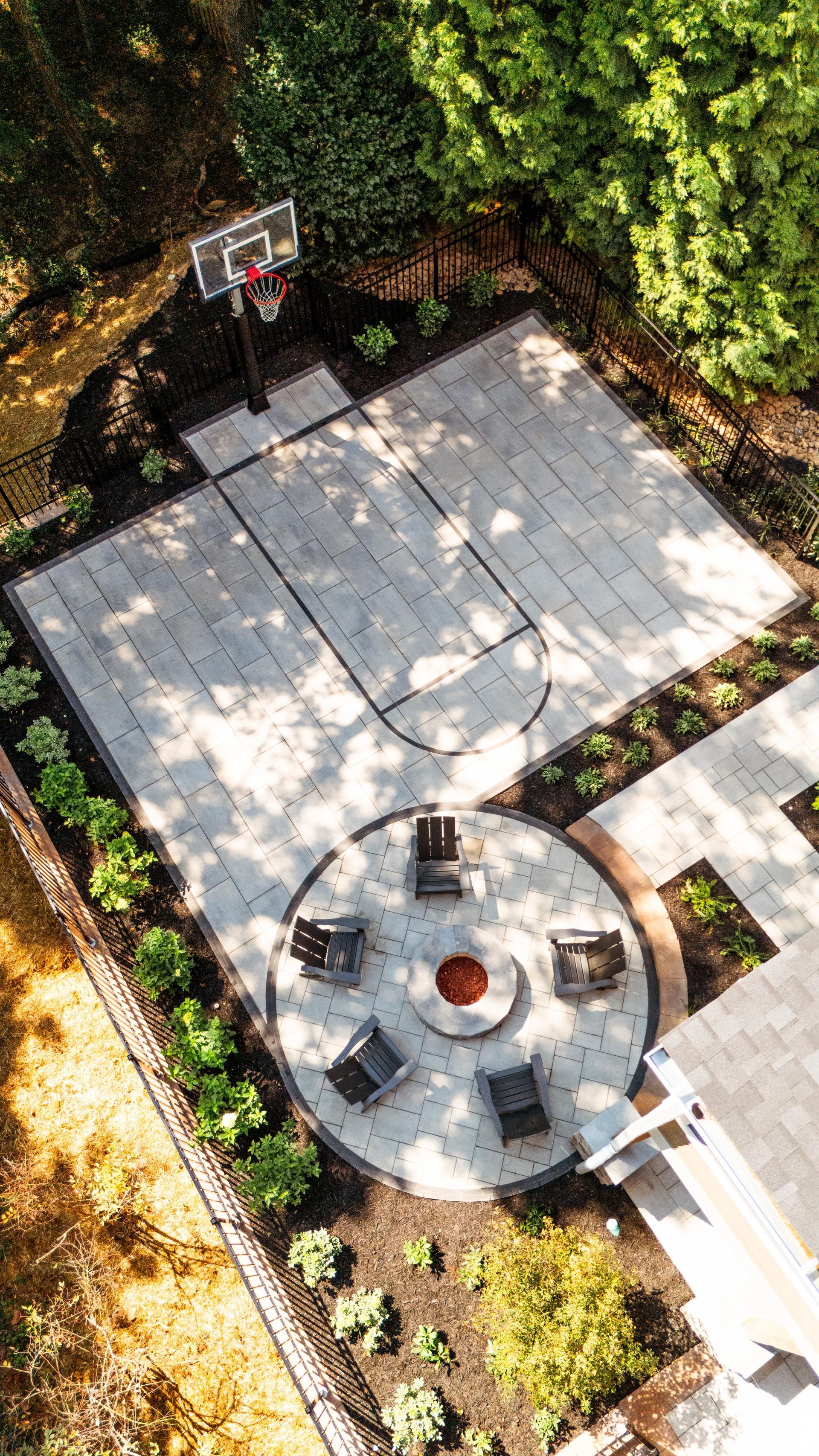 Overhead view of a backyard patio with stone pavers, a circular fire pit, and surrounding trees and plants
