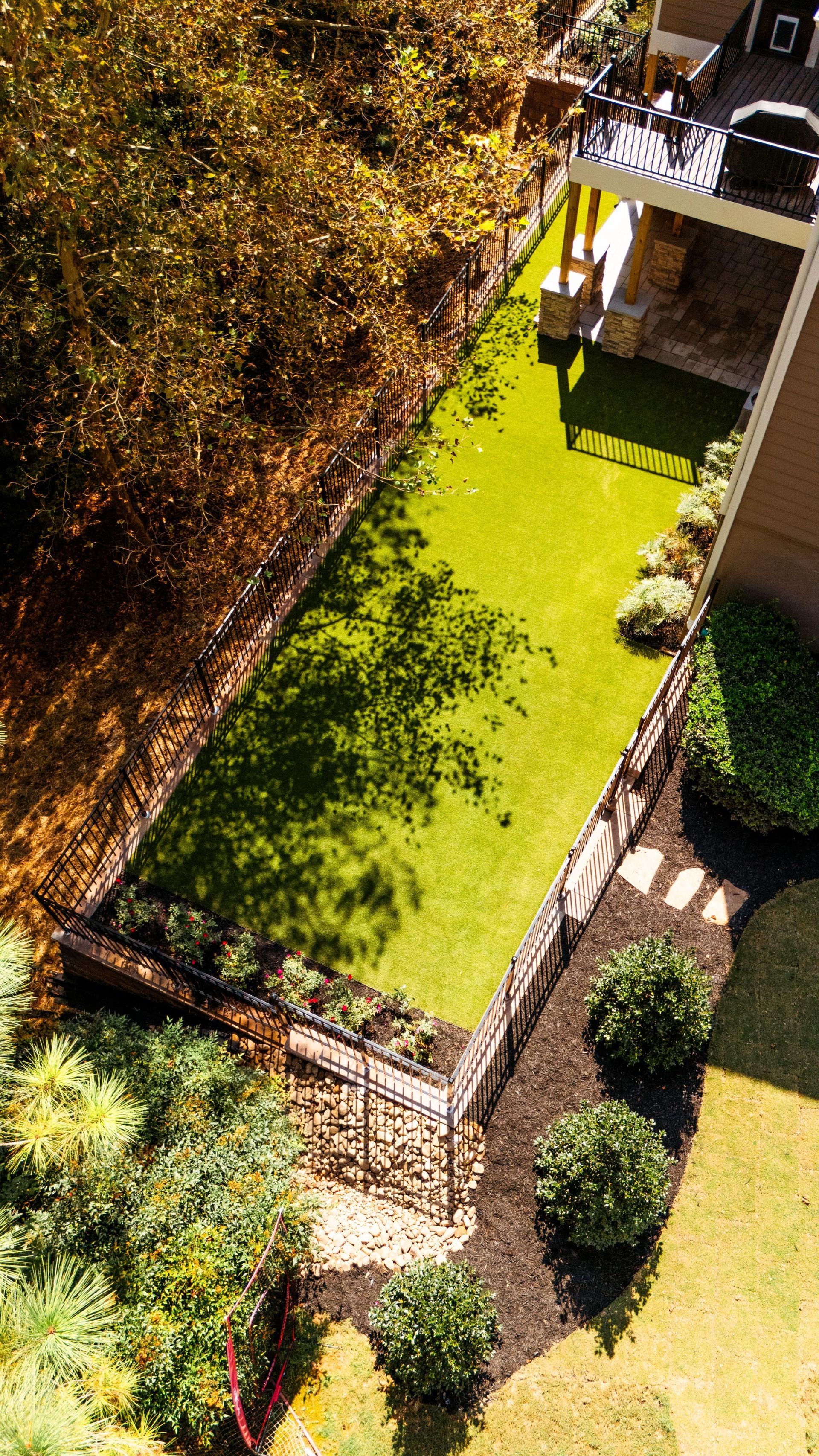 A small rooftop garden with bright green grass, shrubs, and surrounding trees beside a building.