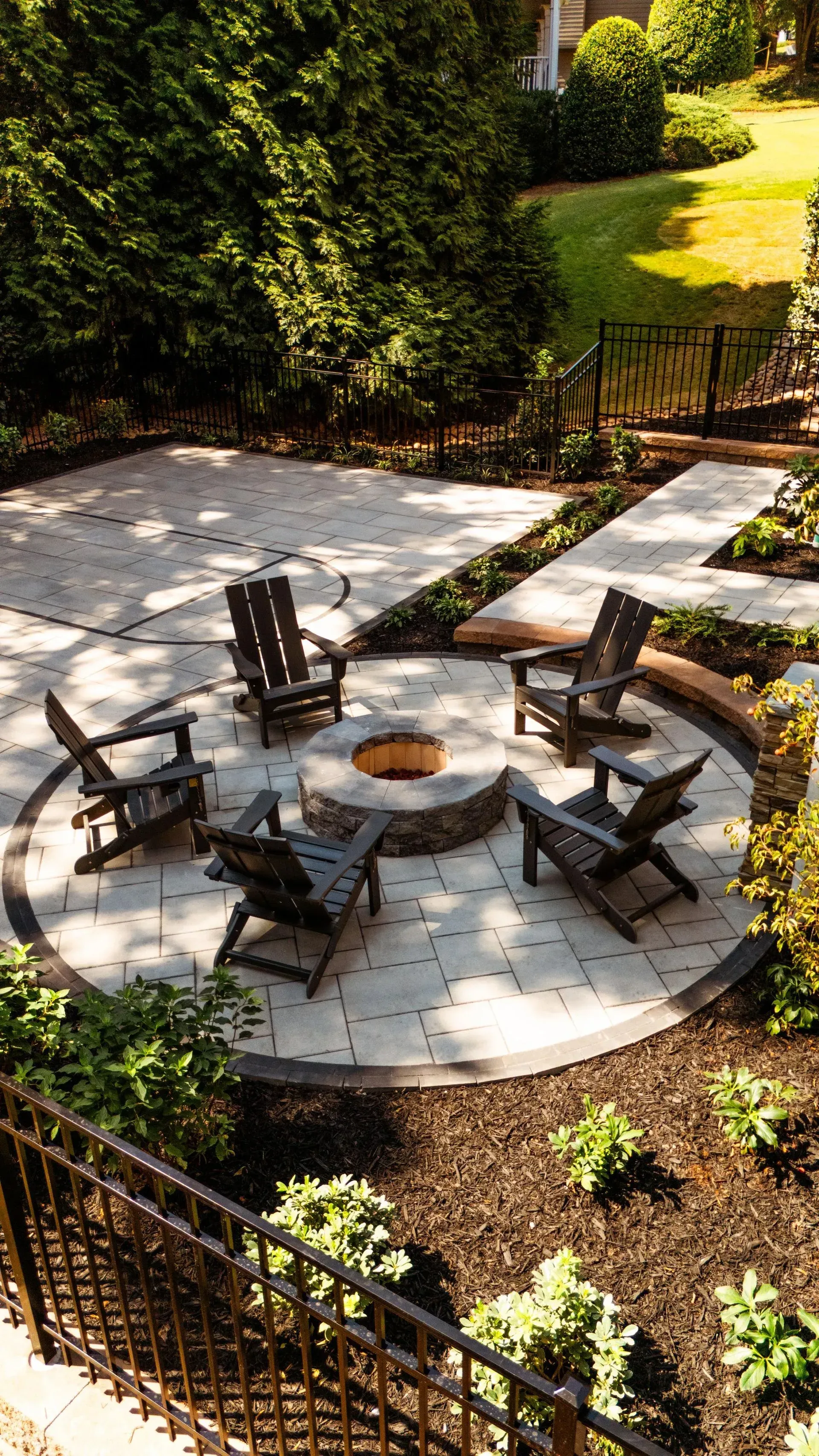 Patio fire pit surrounded by Adirondack chairs in a sunny garden courtyard