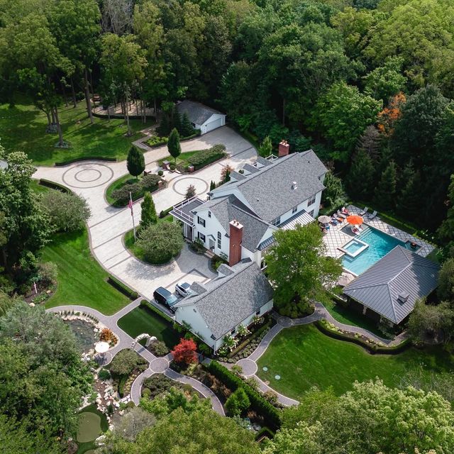 Aerial view of a house with a pool, landscaped gardens, and surrounding trees