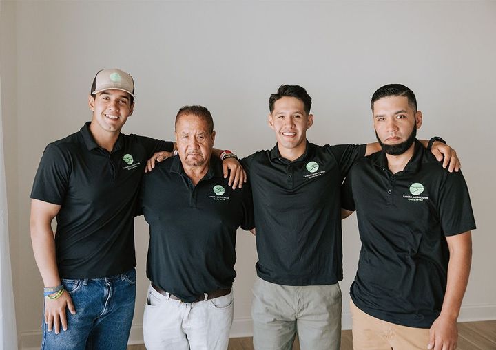 Four people in black polo shirts standing together with arms around each other, smiling indoors.
