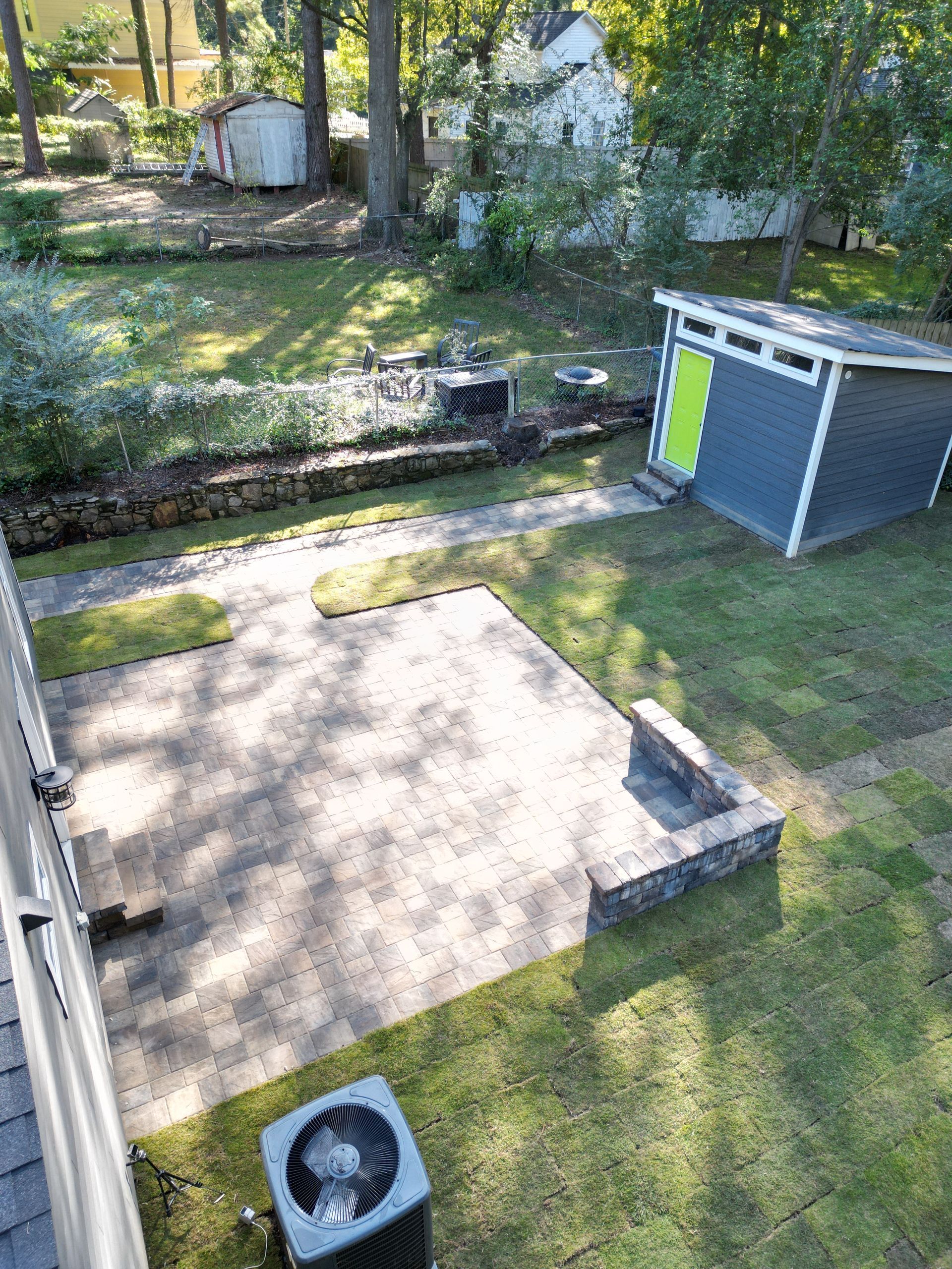 Backyard with a concrete slab, a gray shed, and a small fan on the grass among trees and shrubs