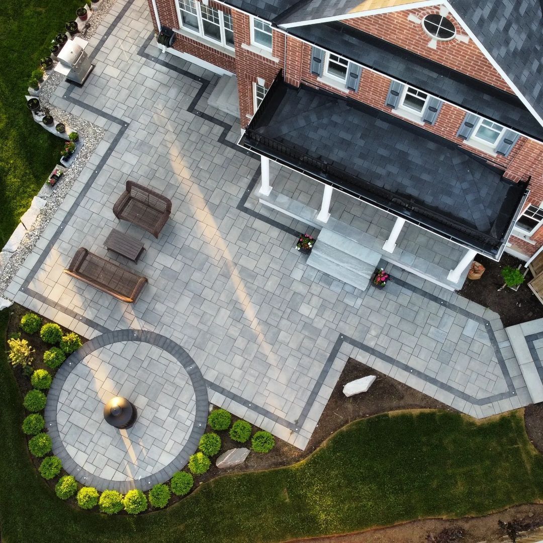 Aerial view of a brick house with a patio, round seating area, and landscaped lawn
