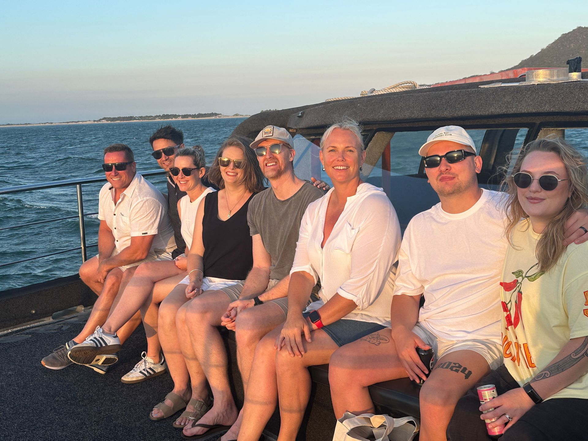 Group of people on a boat, smiling at the camera, ocean in the background.
