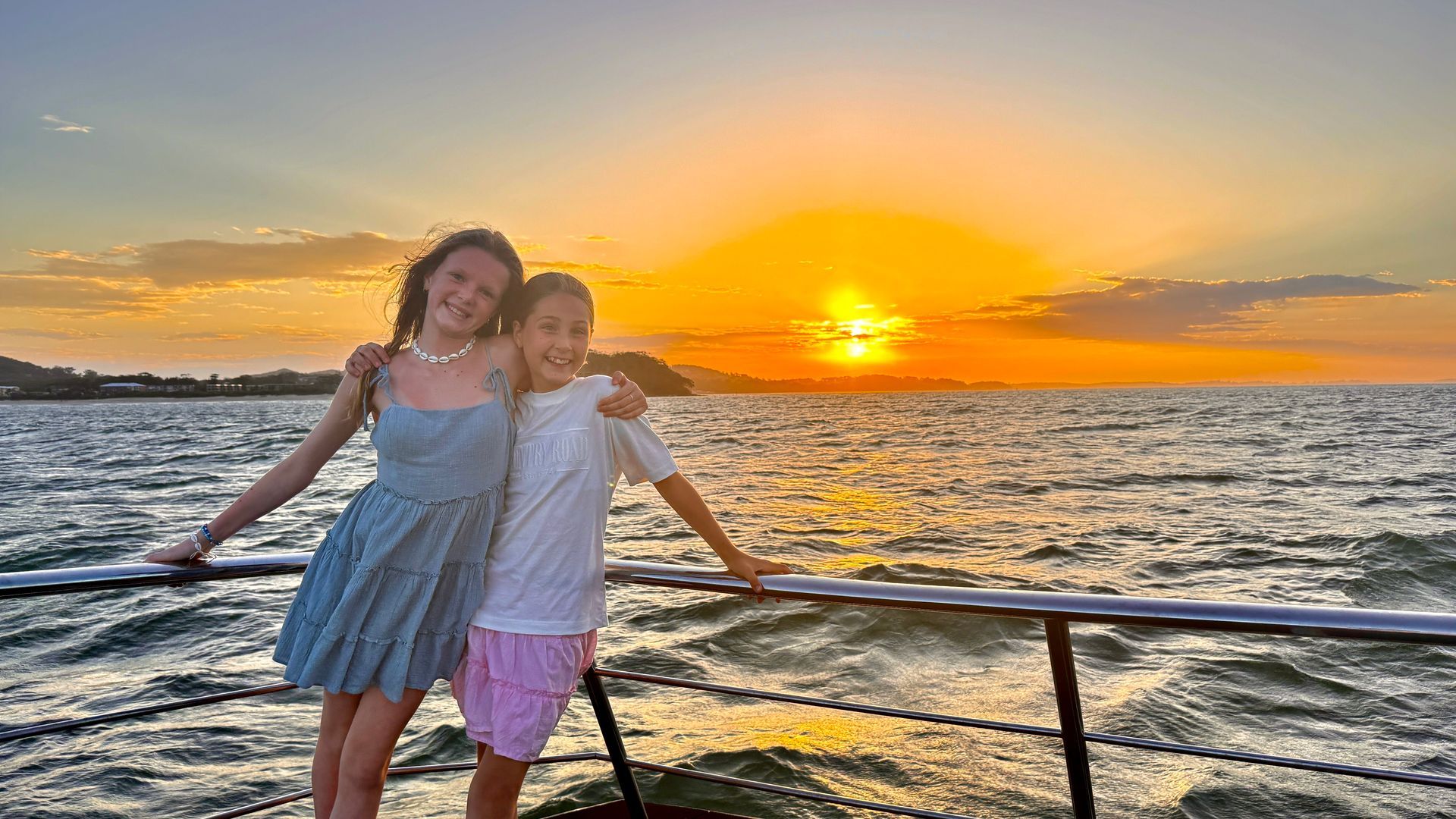 Two people on a boat, arms around each other, watching a sunset over the water.