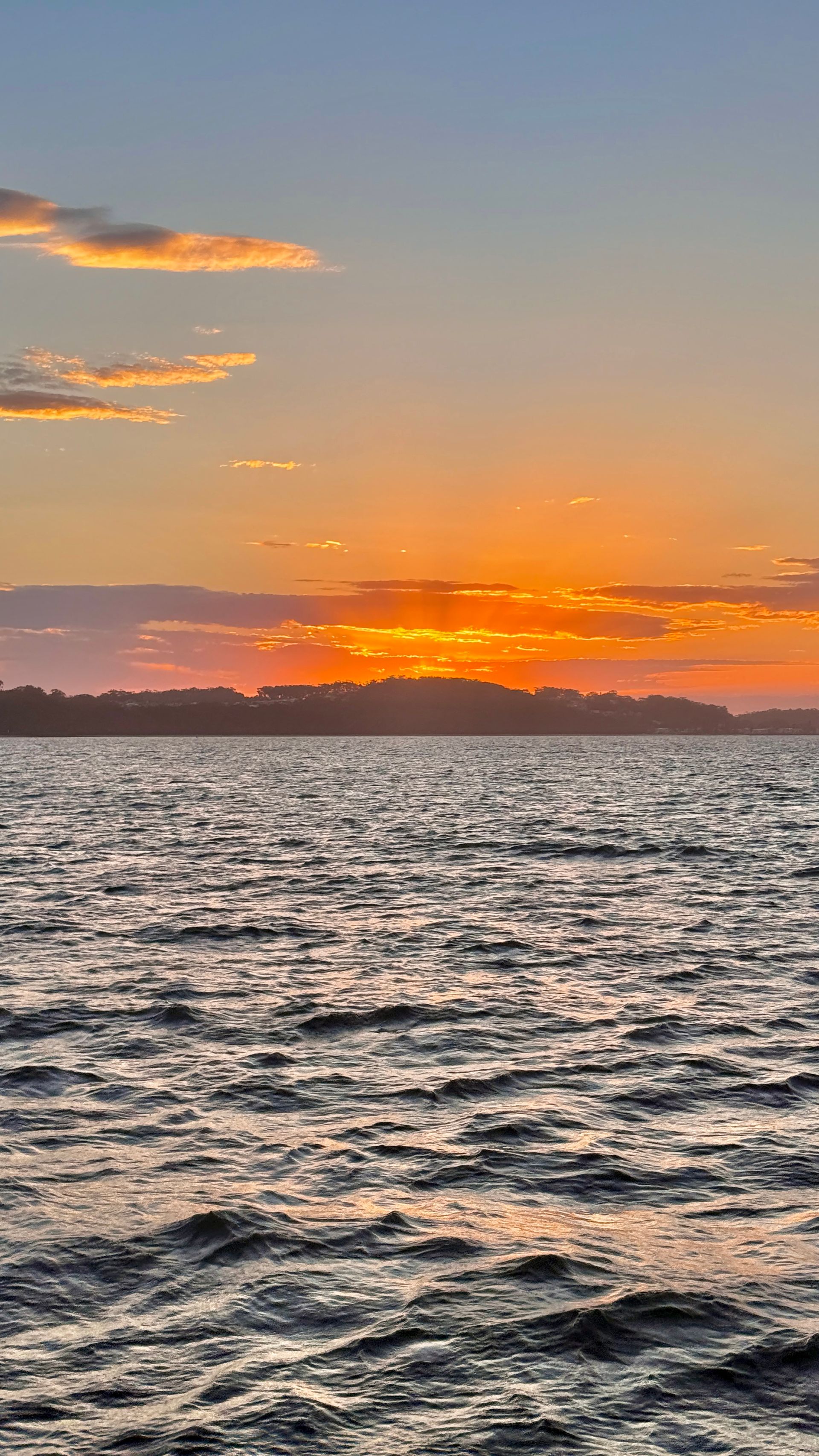 Sunset over a wavy body of water, with orange and blue sky.