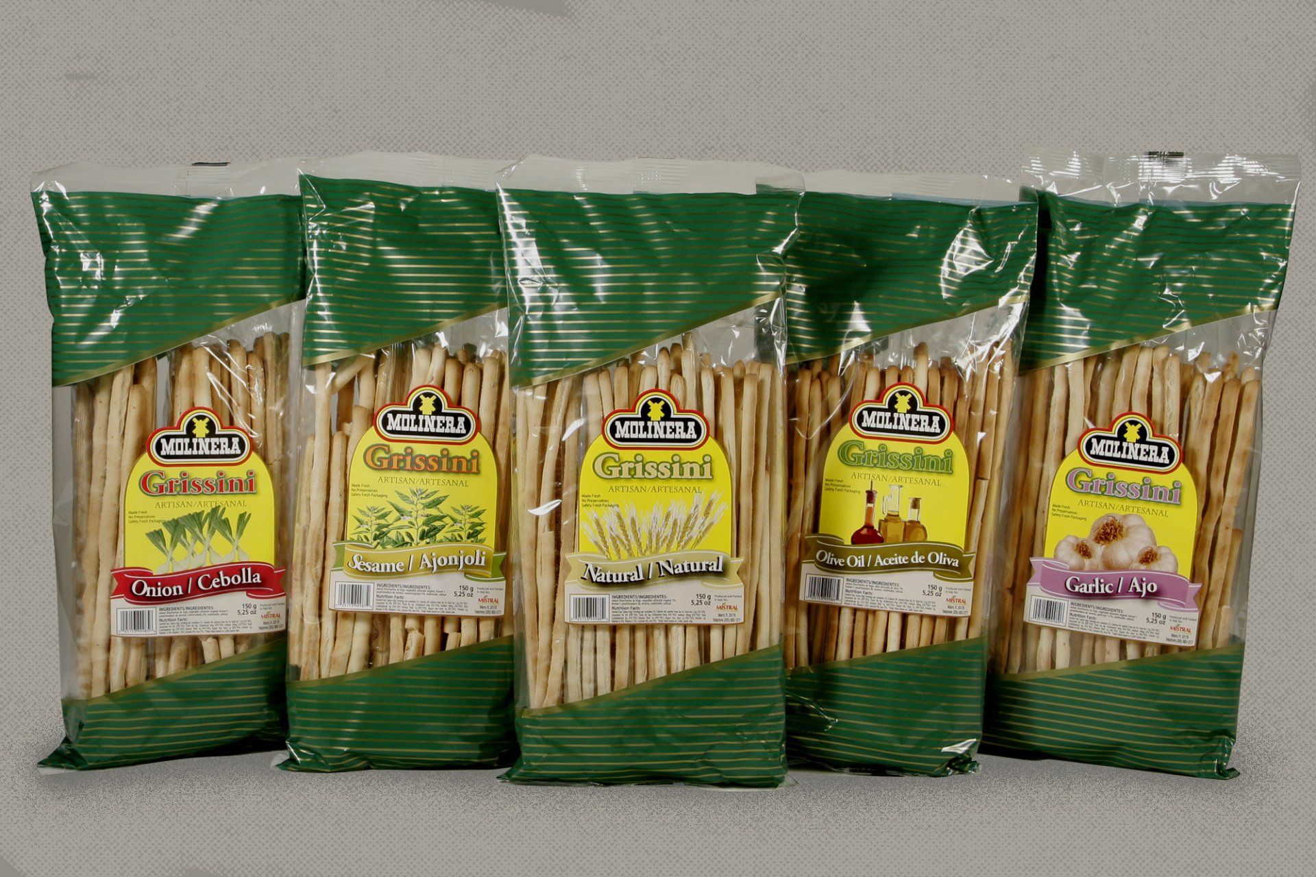 Five bags of packaged breadsticks, each with a different flavoring, stand side-by-side against a neutral backdrop. Each bag features a green top and a yellow and white label.