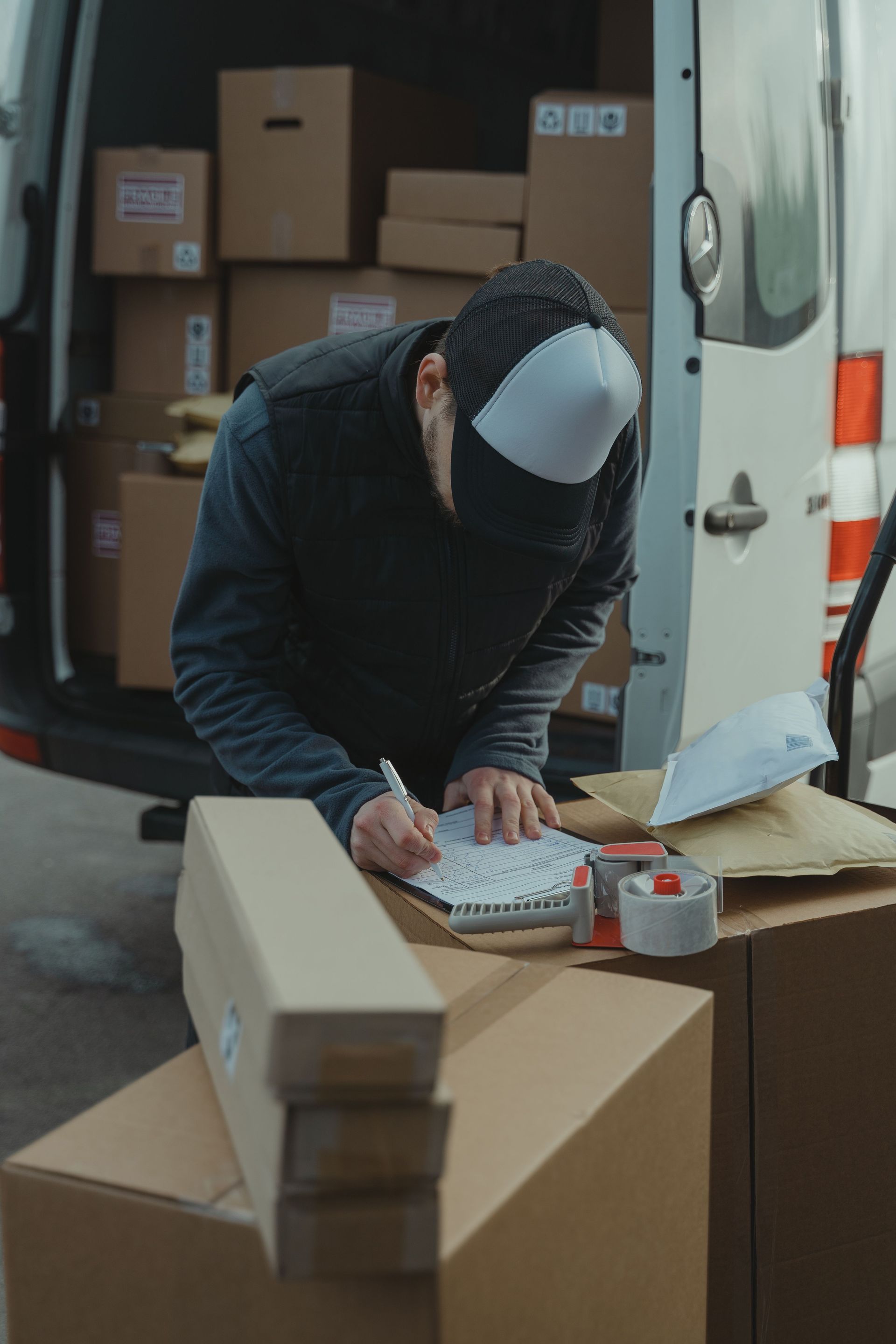 Een persoon schrijft op een klembord in een verhuiswagen, omringd door kartonnen dozen.