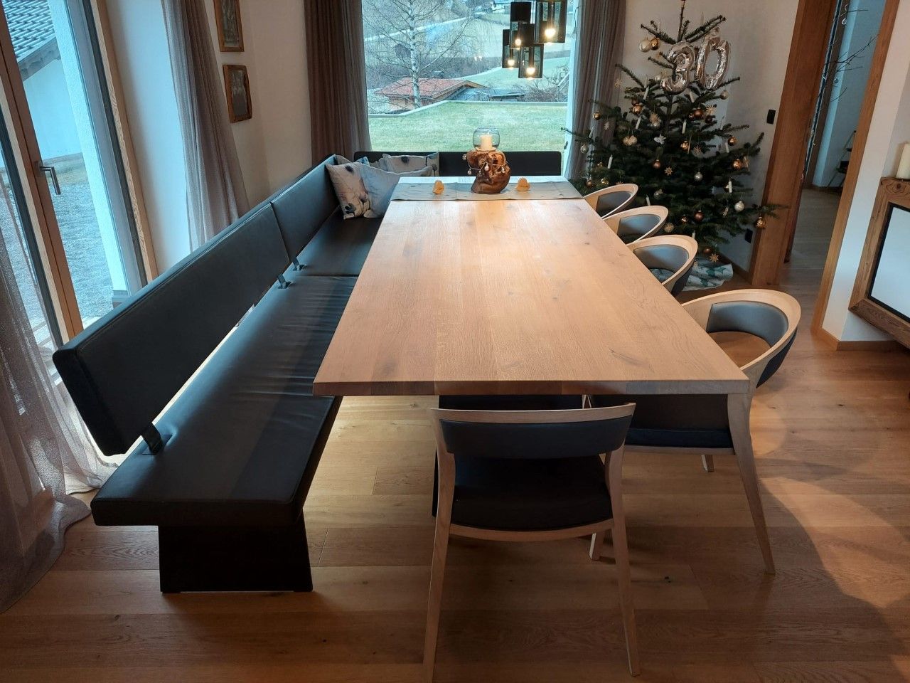 Ein langer Esstisch aus Holz mit schwarzer Eckbank und passenden Stühlen in einem hellen, modernen Esszimmer.