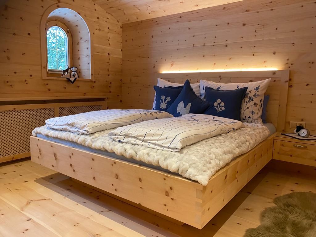 Ein rustikales Schlafzimmer aus Holz mit einem schwebenden Bett, weißer Bettwäsche, blauen Zierkissen und einem Bogenfenster.