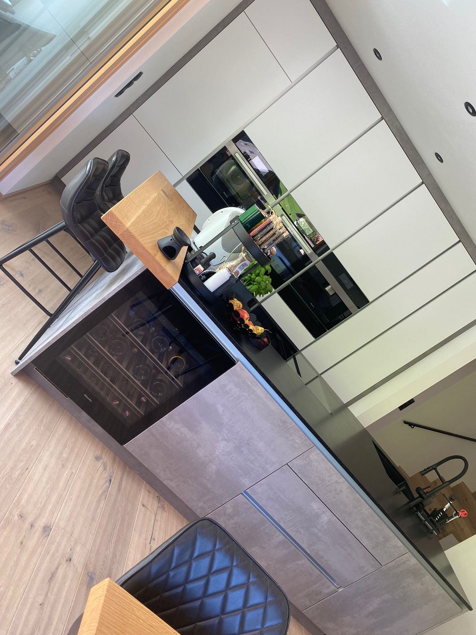 Eine moderne Kücheninsel mit Weinkühlschrank, grauen Schränken, einer Holzarbeitsplatte und Barhockern