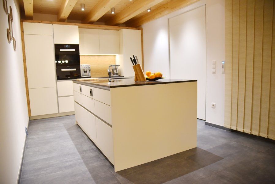 Moderne Küche mit Kochinsel, cremeweißen Schränken, dunklen Arbeitsplatten und hellen Holzbalken an der Decke.