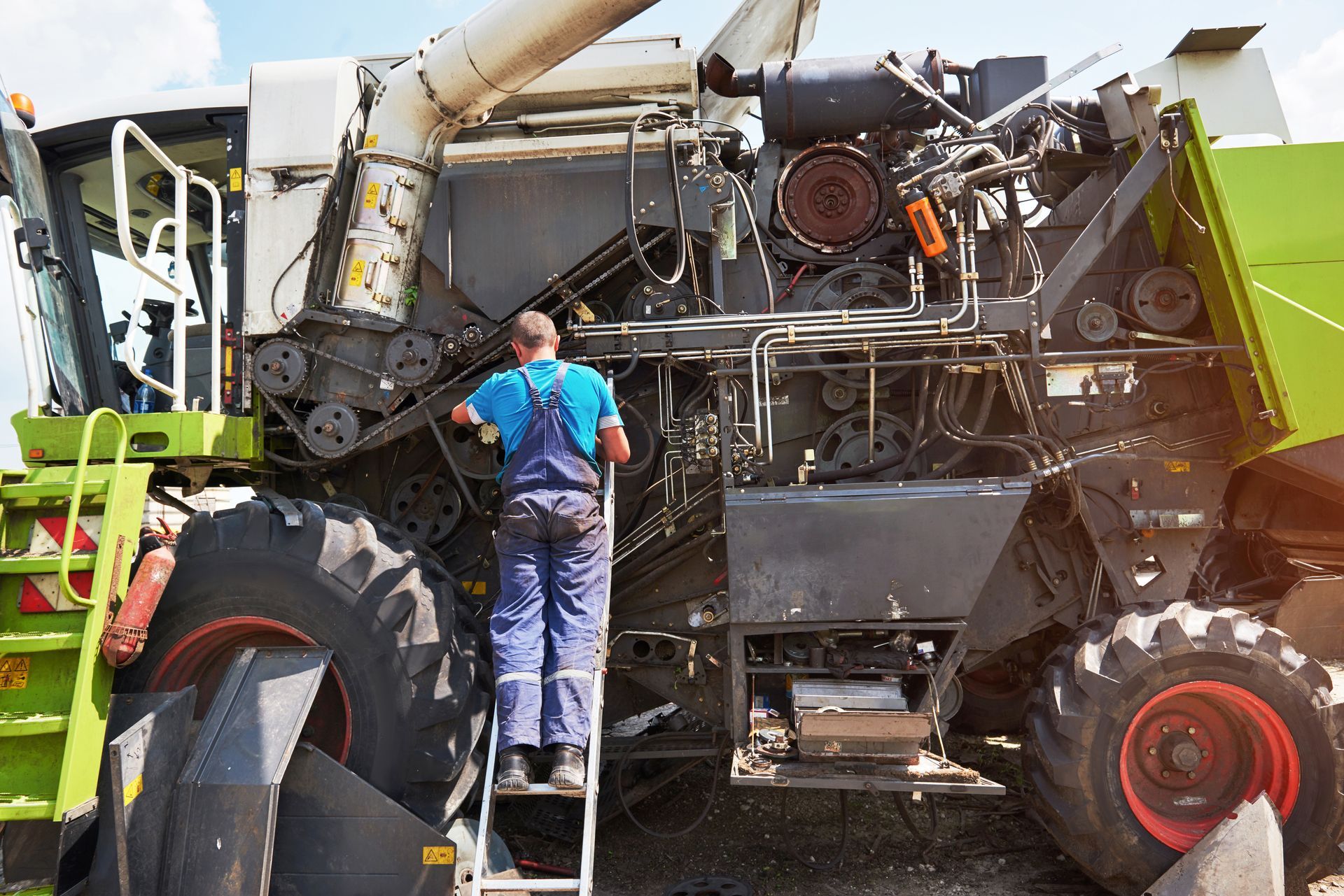 Worker inspecting a large green and white farm machine with exposed machinery and oversized tires