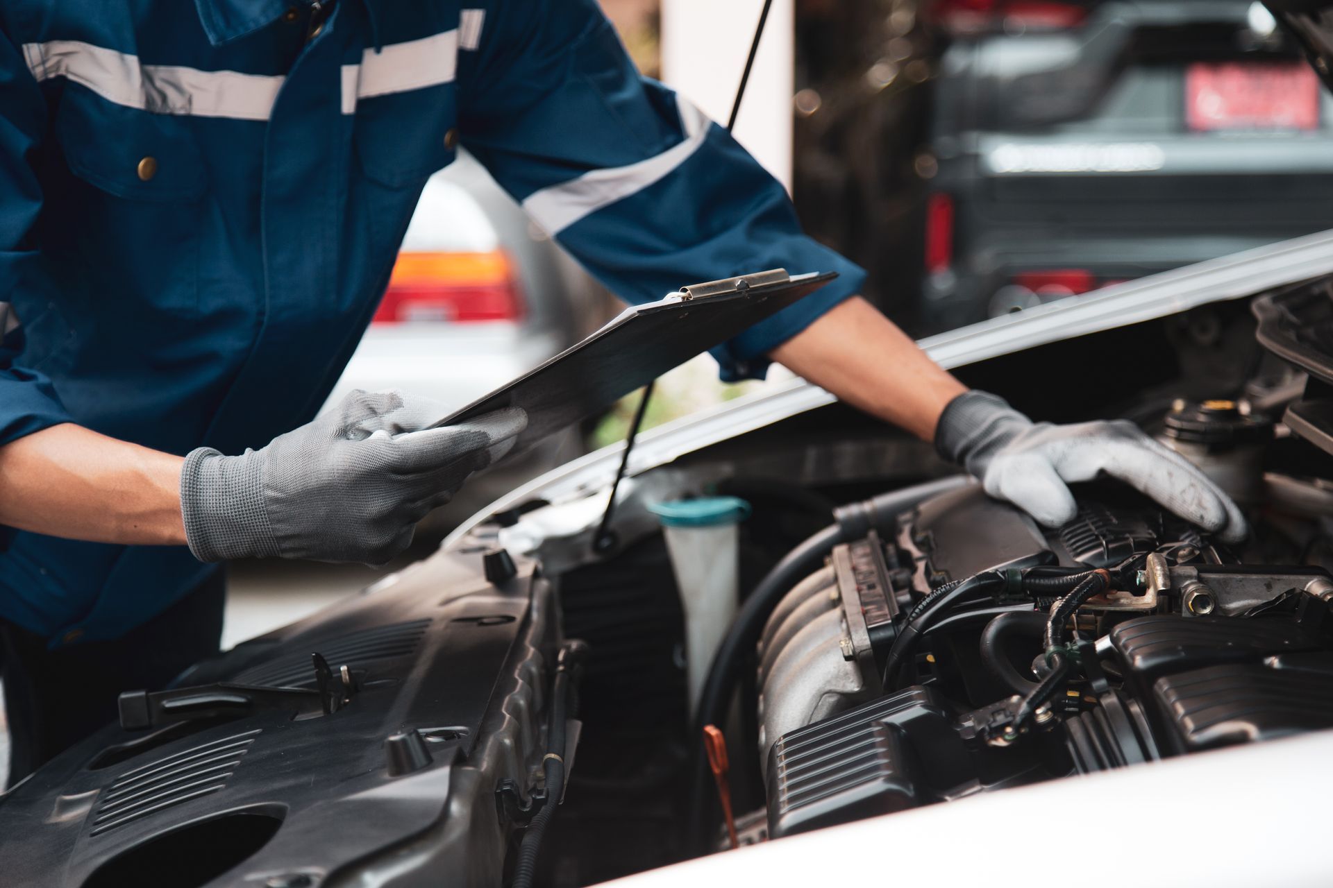 Mechanic checking car engine in a repair shop, wearing gloves and blue uniform