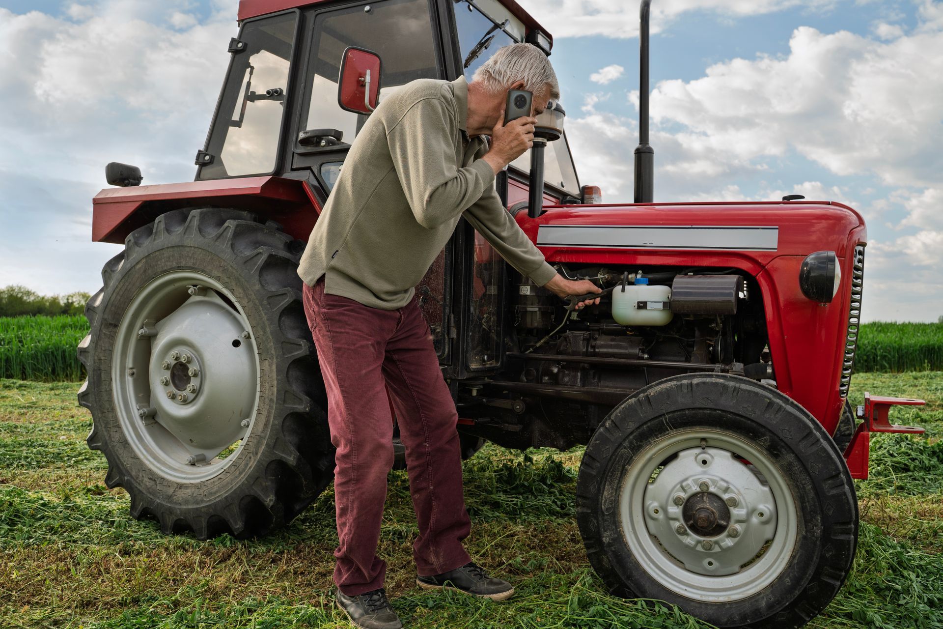 Person inspecting a red tractor in a grassy field under a cloudy sky