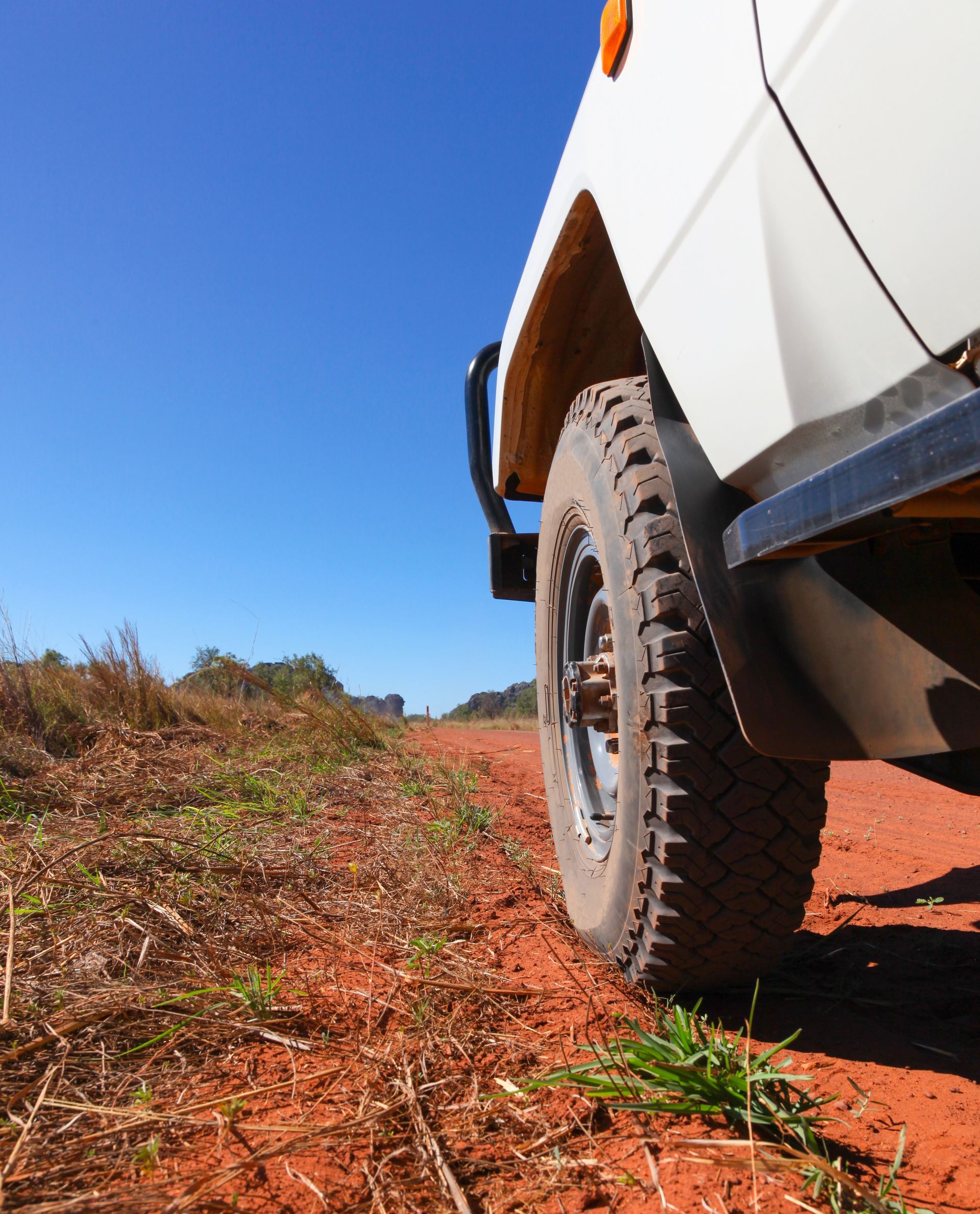 Close-up of a white off-road vehicle tire on a red dirt road under a blue sky