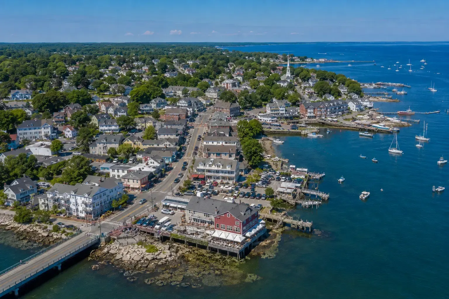 Aerial view of a coastal harbor town with boats, docks, and houses along blue water.