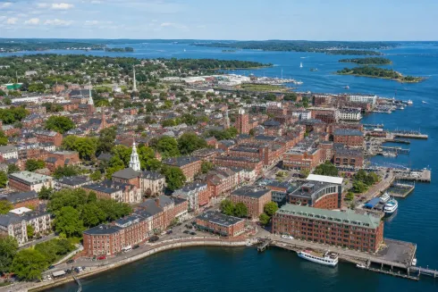 Aerial view of a coastal city with red-roofed buildings, harbor, and blue water