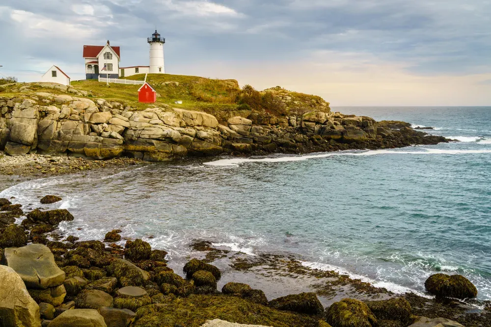 Rocky coastline with a white lighthouse and red-roofed building overlooking the sea