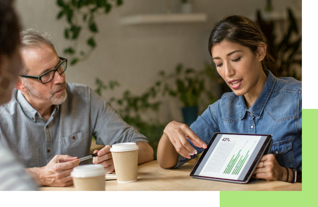 Woman pointing at tablet screen, presenting data to colleagues at a table.
