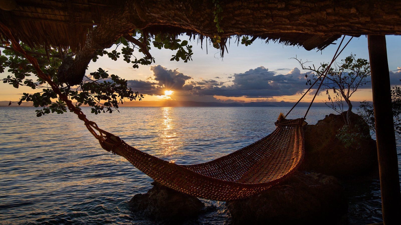 Hammock hanging near ocean at sunset; golden sunlight on the water.