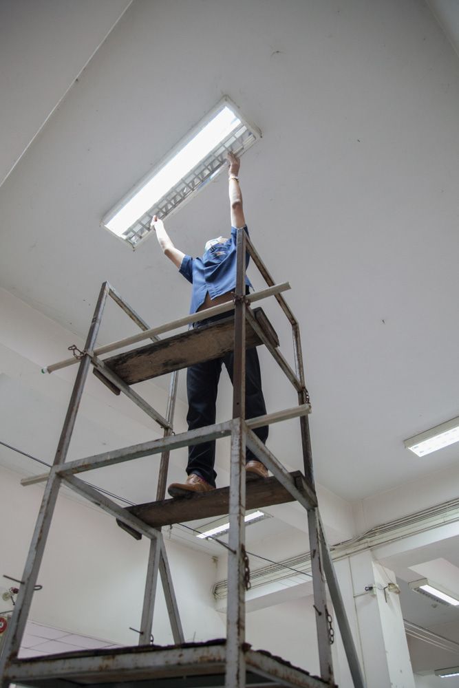 A Man Is Standing On A Ladder Fixing A Light Fixture — In Electrics In Innisfail, QLD